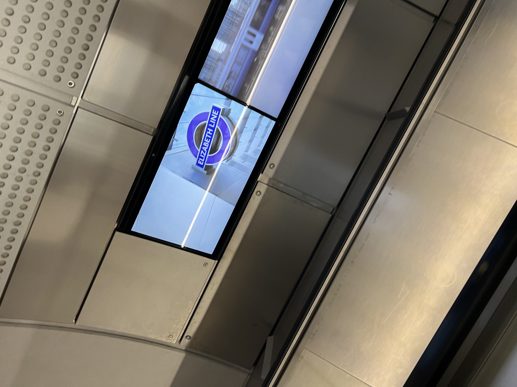 A photo of the displays mounted parallel to an Elizabeth Line escalator